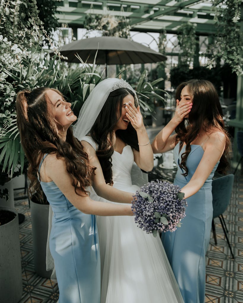 Bride and bridesmaids sharing a joyful moment in an elegant outdoor setting with lush greenery.